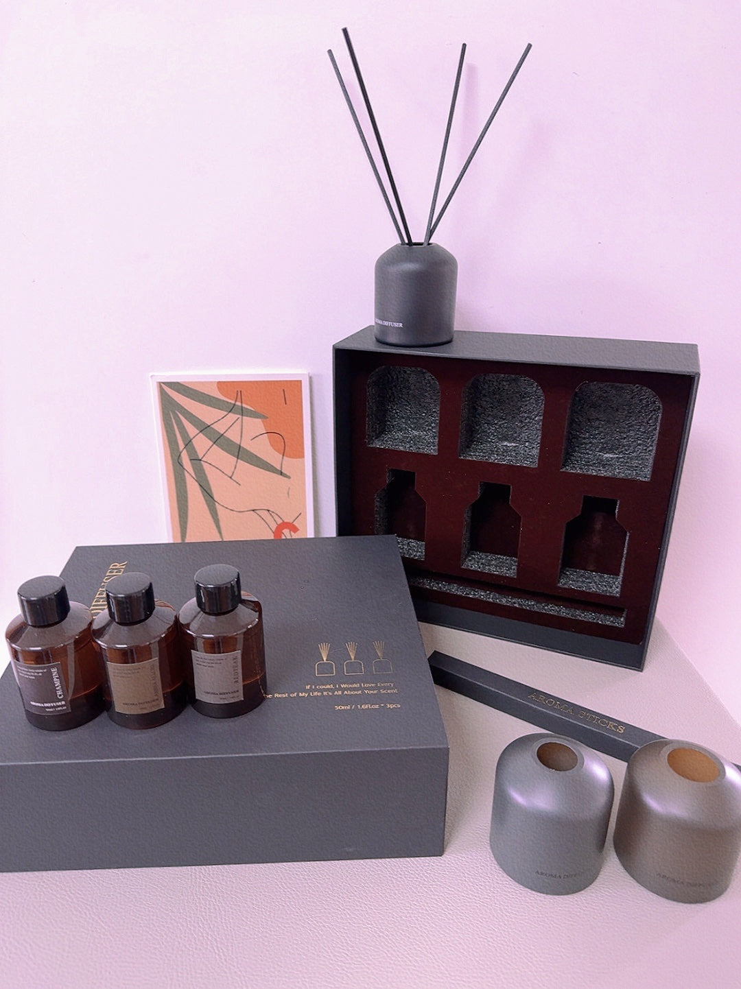 Set of diffusers including bottles, a diffuser stick, and a box on a light pink background