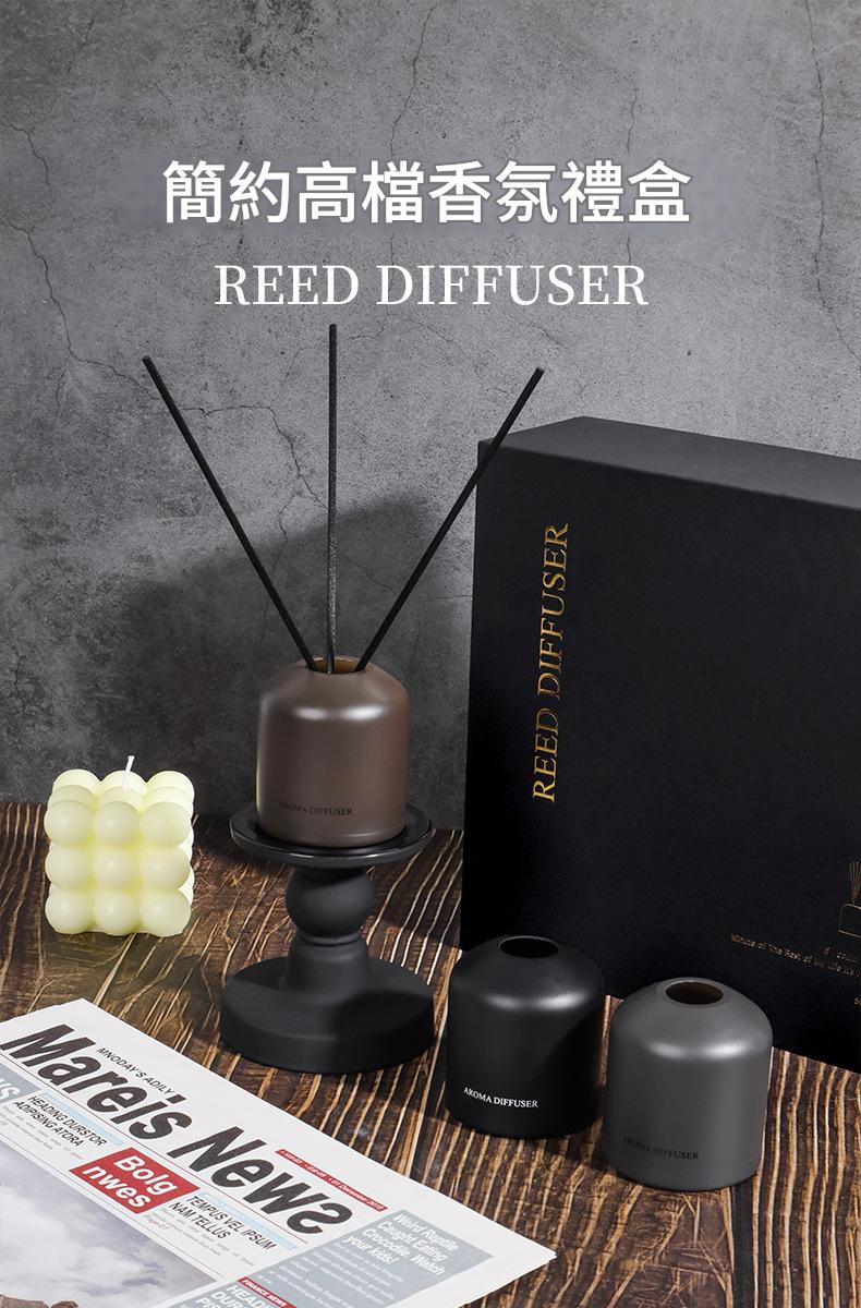 Reed diffuser set with black box, candle, and diffuser on a wooden surface.