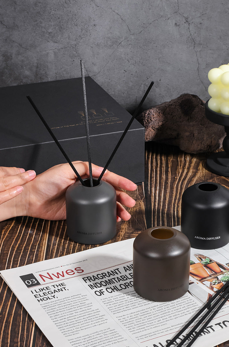Person holding a diffuser with black reeds on a wooden surface with a magazine and decorative items.