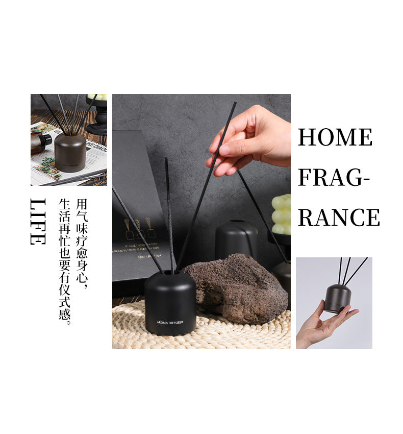 Black home fragrance diffuser with sticks on a textured surface, surrounded by decorative elements.