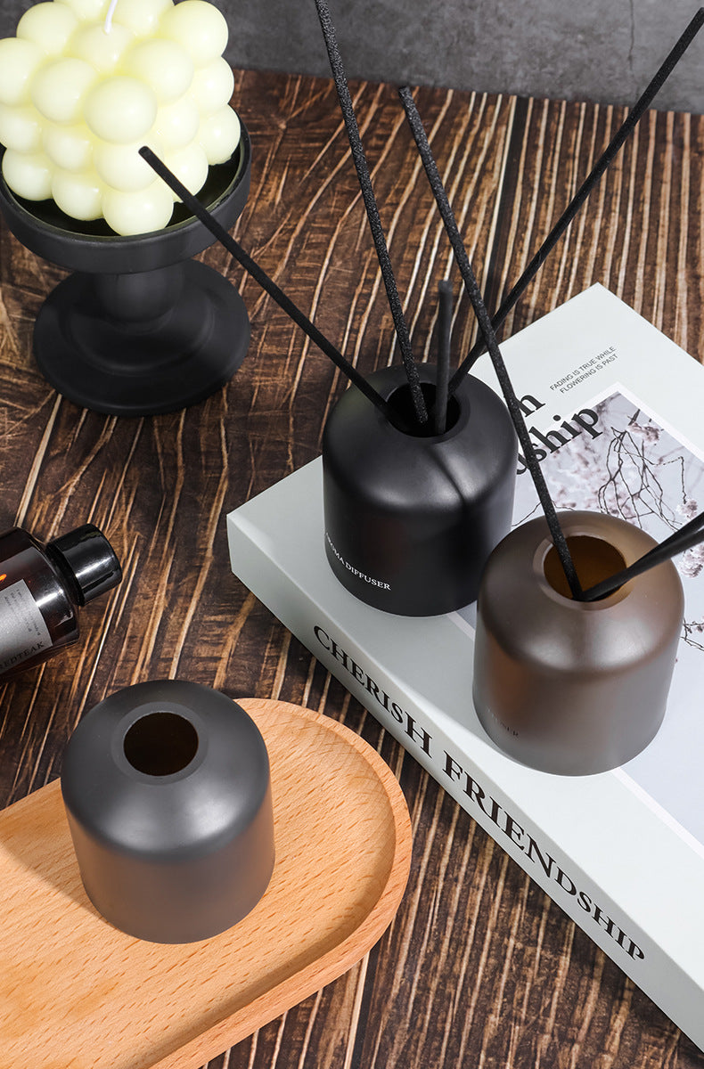 Diffuser with reeds on a wooden surface with a book and candle in the background