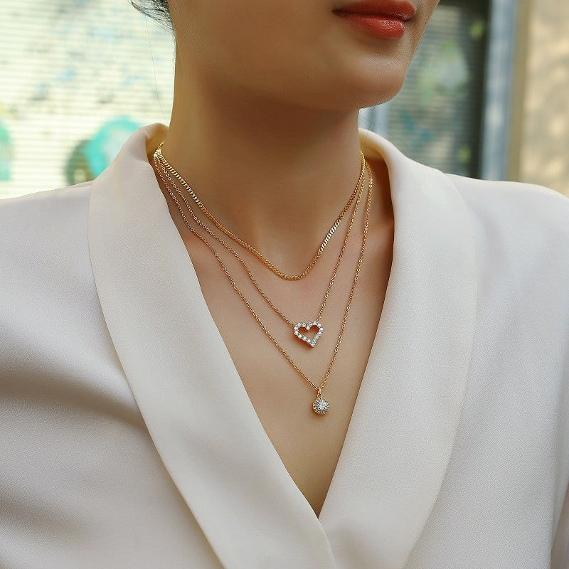 Woman wearing a gold necklace with a heart-shaped pendant in front of a blurred outdoor background