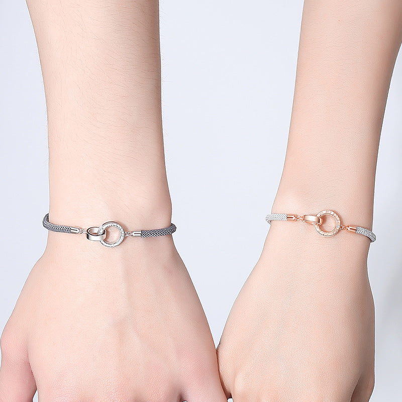 Two wrists wearing silver bracelets with circular designs on a light gray background