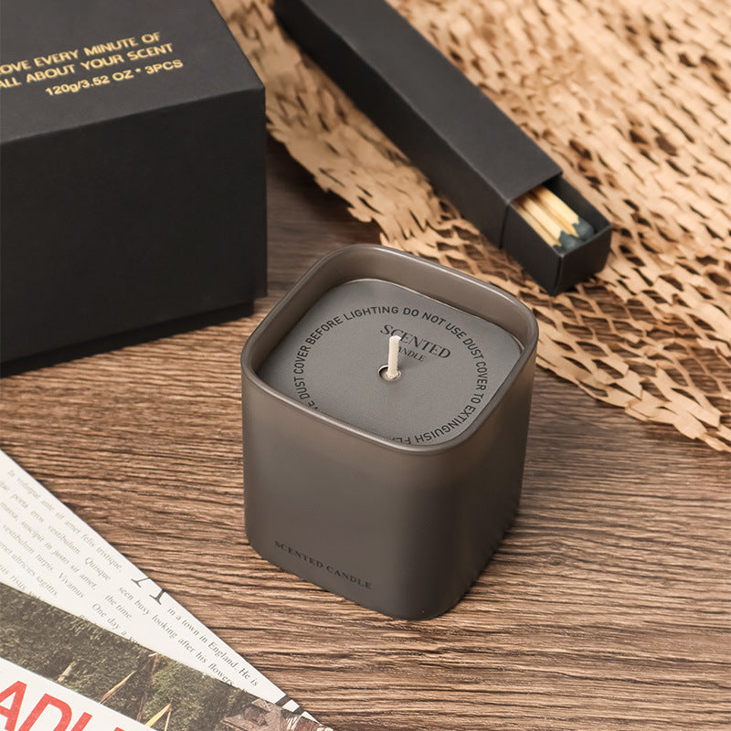 Dark gray candle with wooden wick on a textured surface, with a black box and matches in the background.