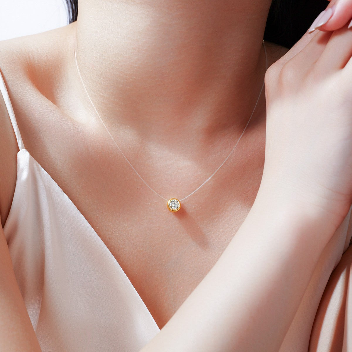 Close-up of a delicate necklace with a small pendant on a person wearing a white top.