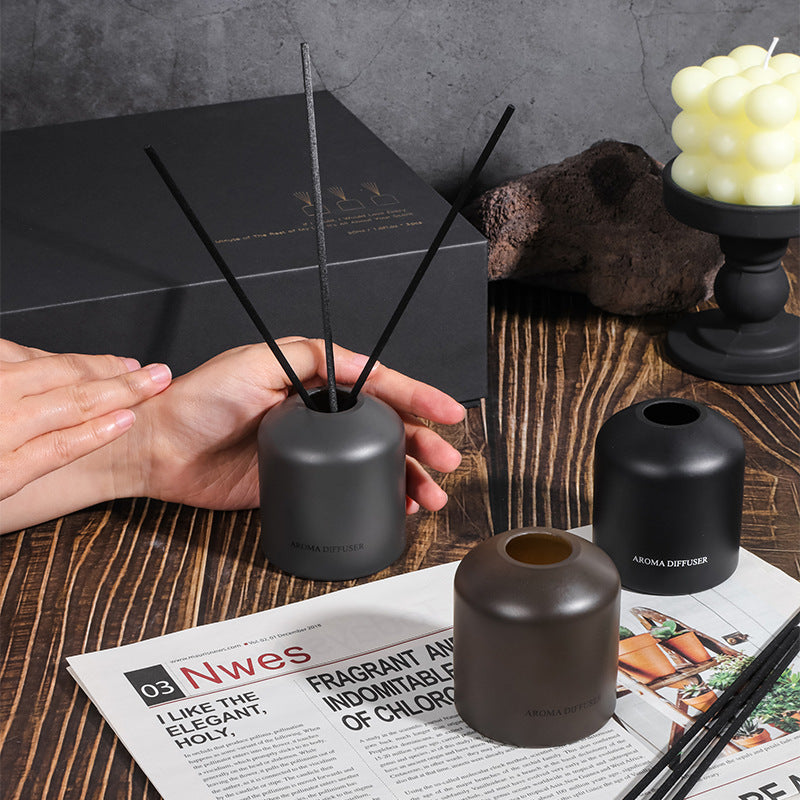 Person holding a black diffuser with reeds on a wooden surface with other diffusers and a candle.