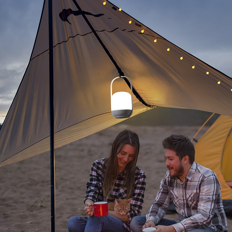 Two people sitting under a tent with a hanging light, on a beach.