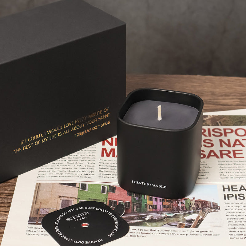 Black scented candle in a container on a newspaper with a black box in the background