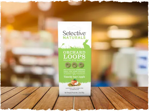 Selective Naturals Orchard Loops pet food package on a wooden surface with a blurred background