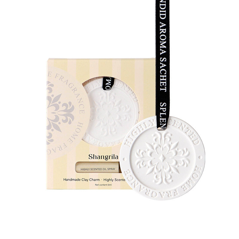 White clay charm with 'Shangrila' text on a beige box with brand name.