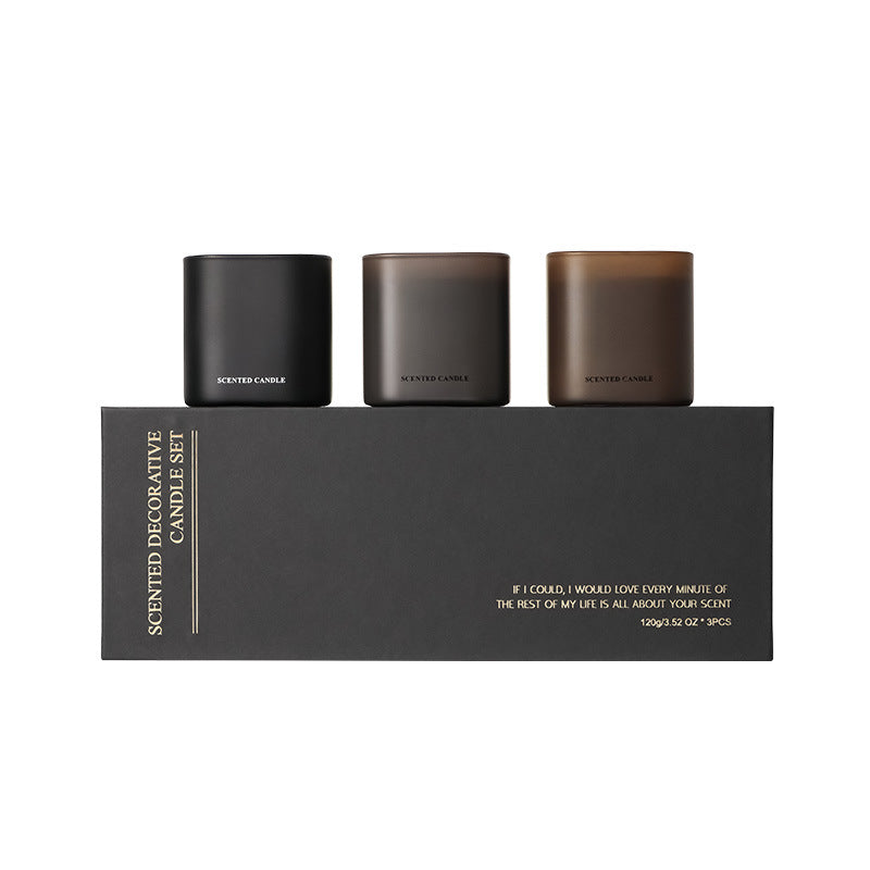 Set of three scented candles in black containers on a black box with text.