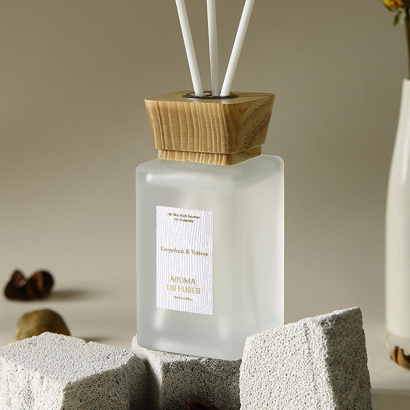 Frosted diffuser bottle with wooden cap on a stone surface, blurred background