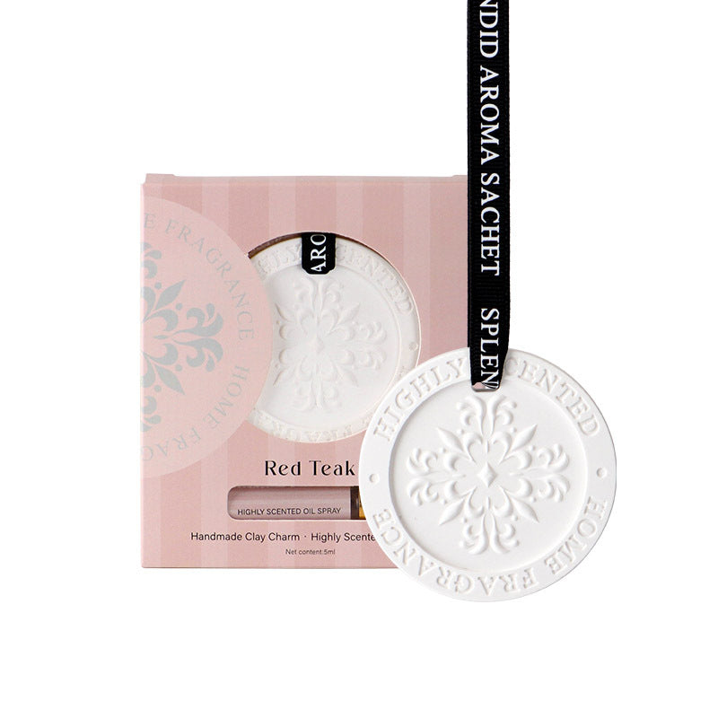 White clay charm with 'Red Teak' text on a pink packaging background