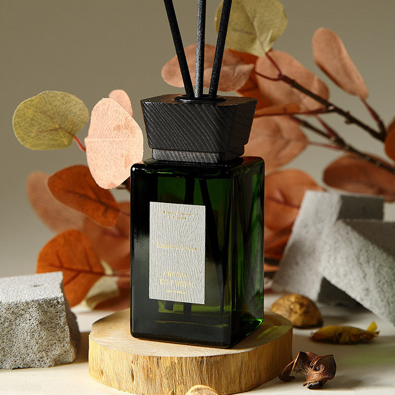 Green diffuser with decorative sticks on a wooden stand against a natural background