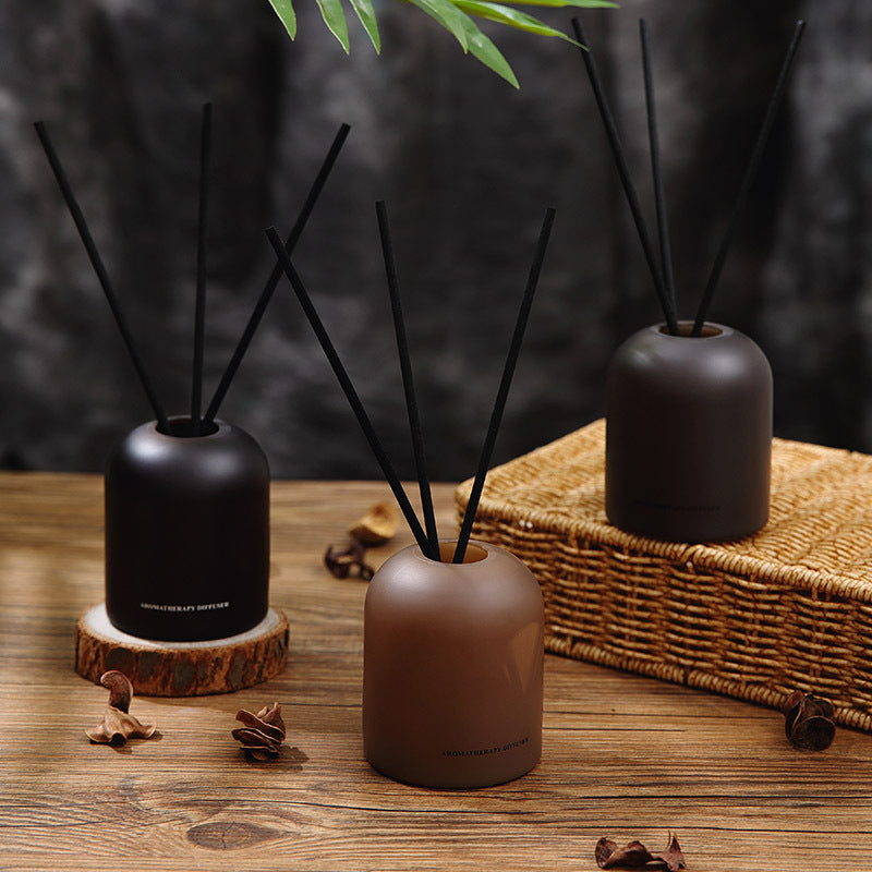 Three diffusers with black sticks on a wooden surface and wicker basket in the background