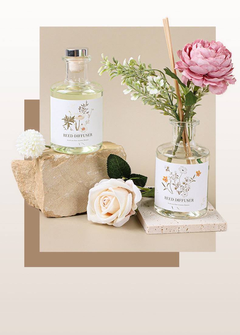 Two glass diffusers with floral labels on a beige surface with flowers.