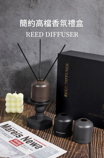 Reed diffuser set with black box, candle, and diffuser on a wooden surface.