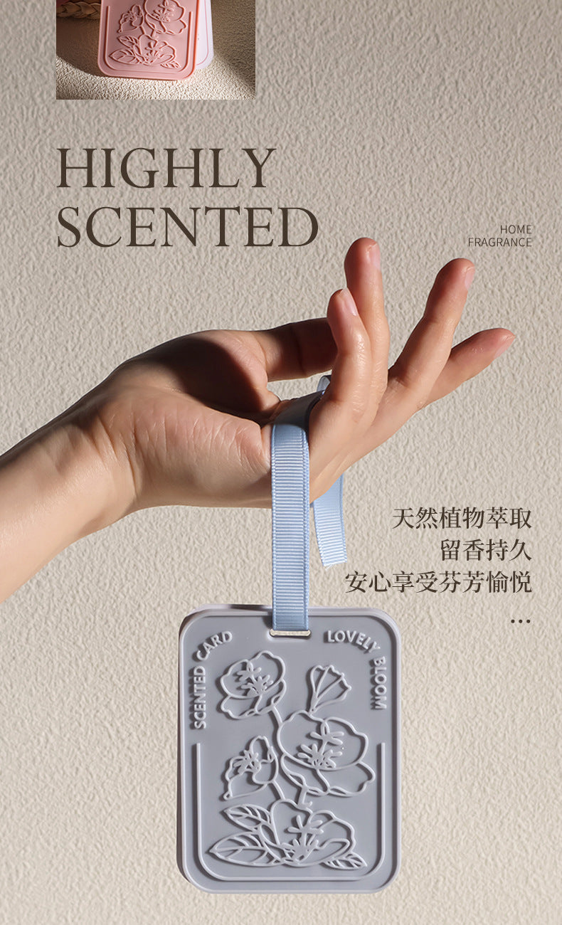 Hand holding a scented luggage tag with floral design against a beige background