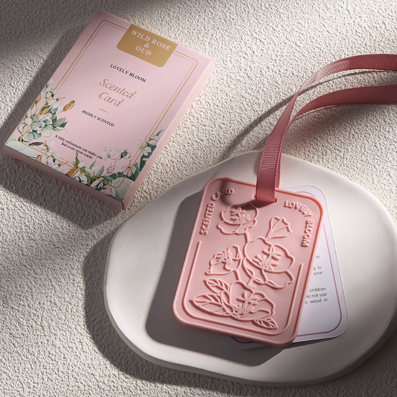 Pink scented card with floral design and ribbon on a textured surface