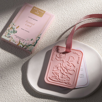 Pink scented card with floral design and ribbon on a textured surface