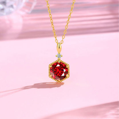 Gold necklace with a red gemstone pendant on a pink background