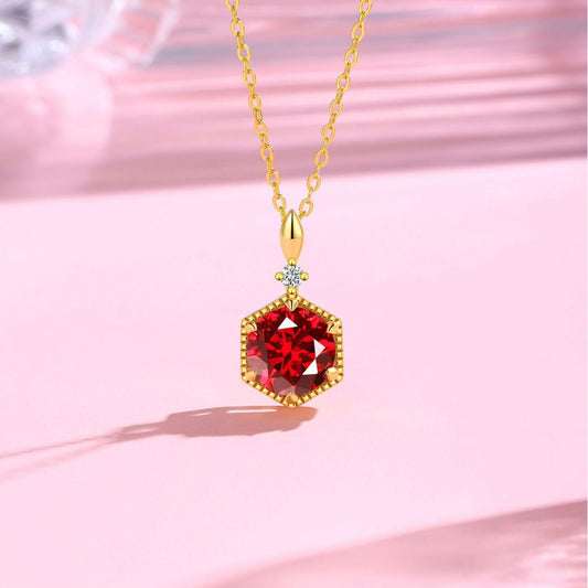 Gold necklace with a red gemstone pendant on a pink background