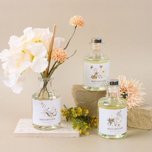 Three glass bottles with floral labels on a beige surface with flowers and stones.