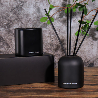 Black scented candle and diffuser set on a wooden surface with a textured gray wall background.