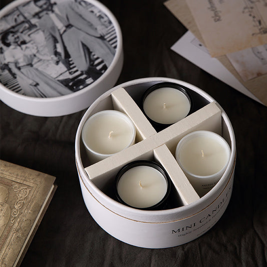 Set of four mini candles in a round white container on a dark surface.
