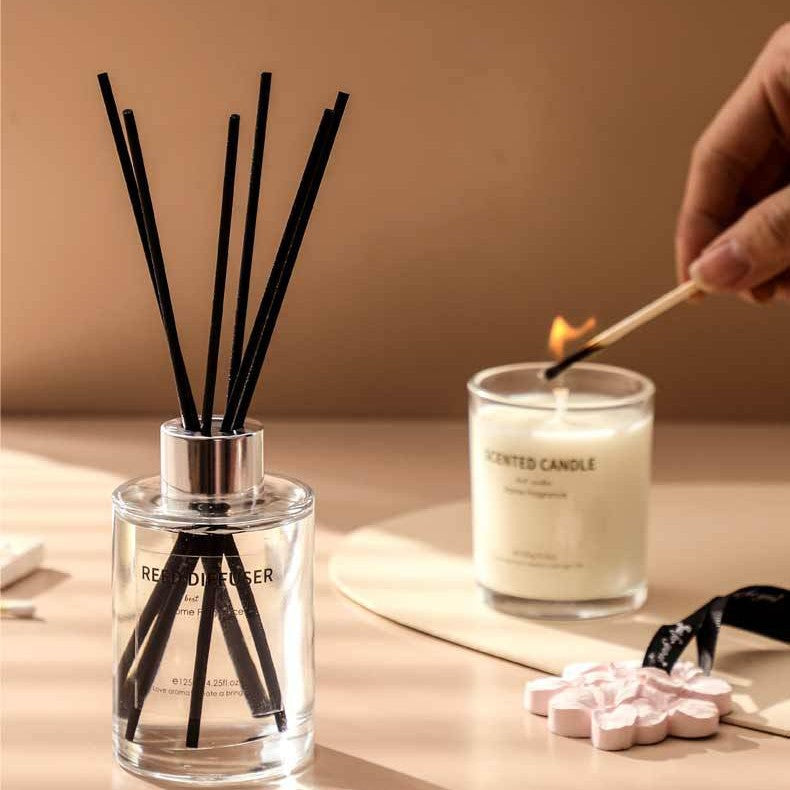 Reed diffuser and candle with a hand lighting the candle on a neutral background