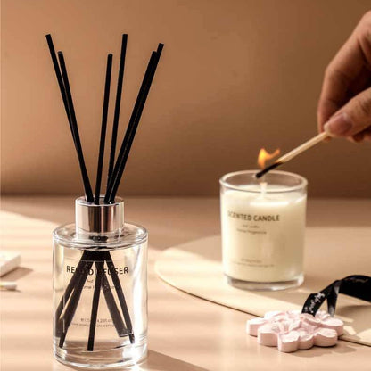 Reed diffuser and candle with a hand lighting the candle on a neutral background