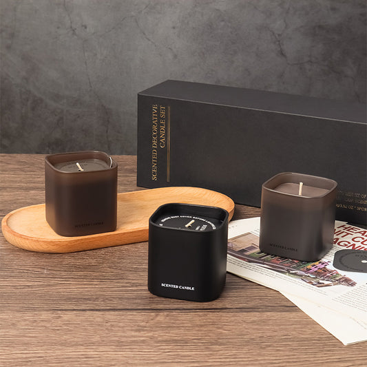 Three scented candles on a wooden surface with a black box in the background.