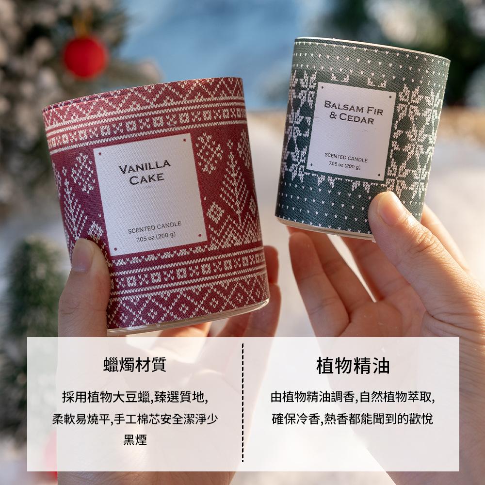 Two scented candles with decorative labels held by hands against a blurred natural background.