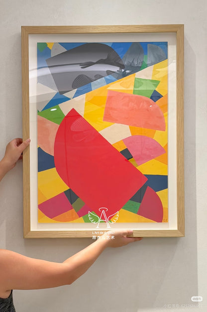 Person holding a colorful abstract art print in a wooden frame against a white wall.