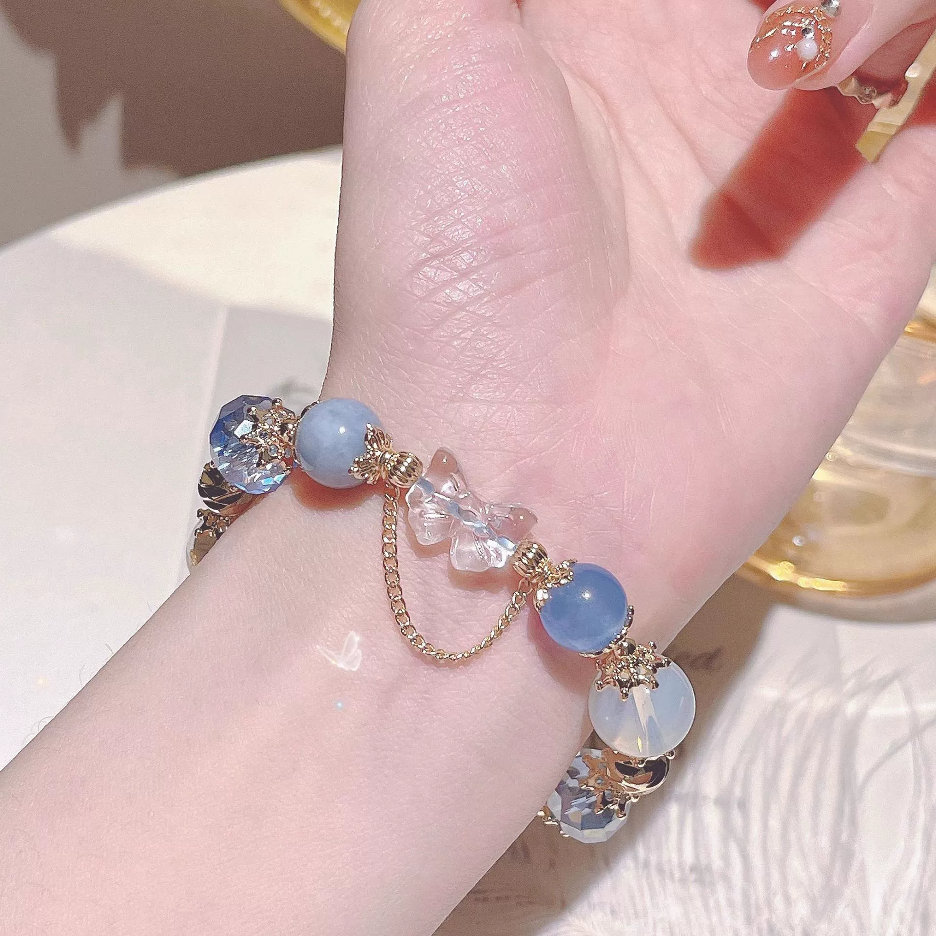 Close-up of a hand wearing a bracelet with blue and clear beads on a neutral background