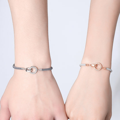 Two wrists wearing silver bracelets with circular designs on a light gray background