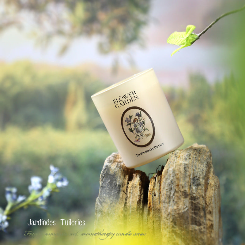 Candle labeled 'Flower Garden' by Jardindes Tuileries on a wooden stump with a blurred natural background.