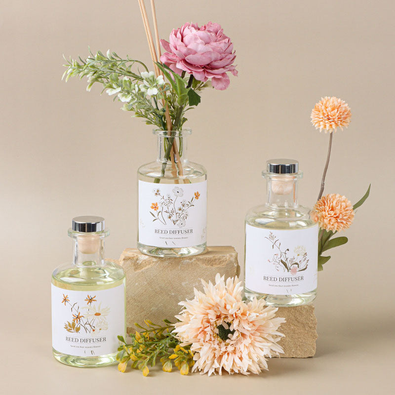 Three glass diffusers with floral arrangements on a beige background