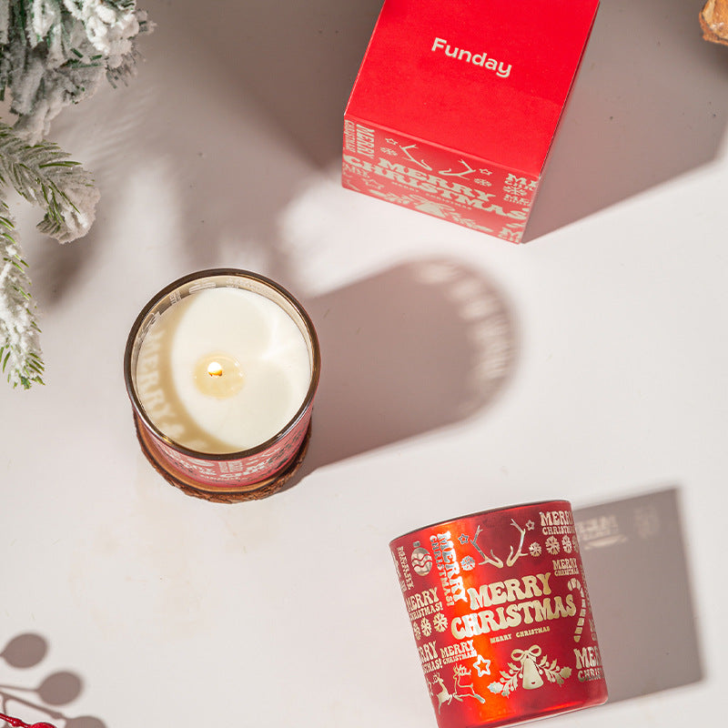 Candle in a decorative container with 'Merry Christmas' text, next to a red 'Funday' box on a light surface.