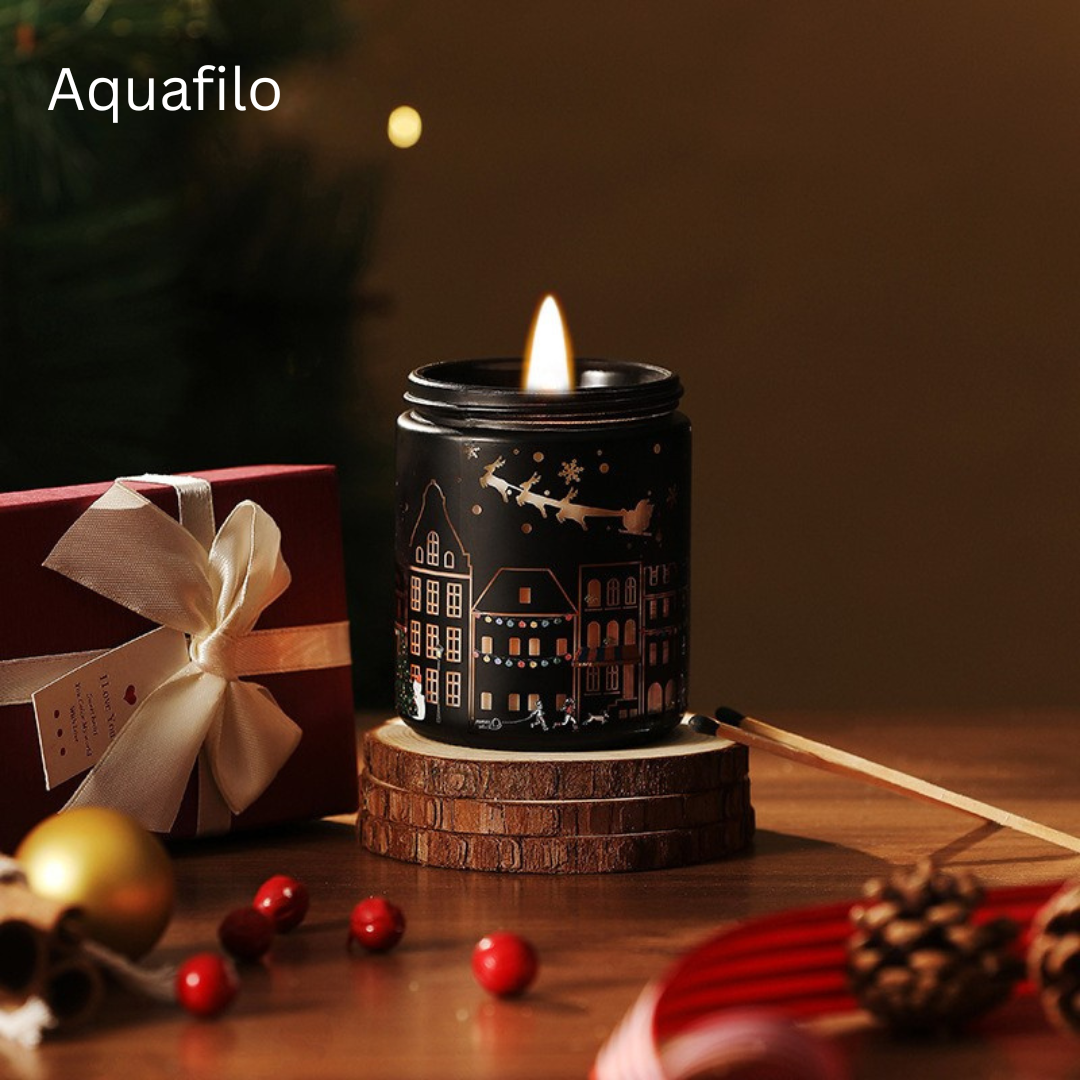 Decorative candle with house design on a wooden base, surrounded by Christmas decorations.