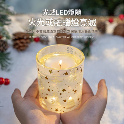 Candle in a glass holder with star patterns held by a hand, surrounded by Christmas decorations.