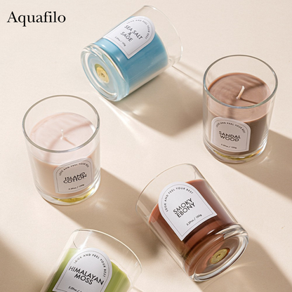 Five scented candles in glass jars with labels on a light beige background, featuring the brand 'Aquafilo'.
