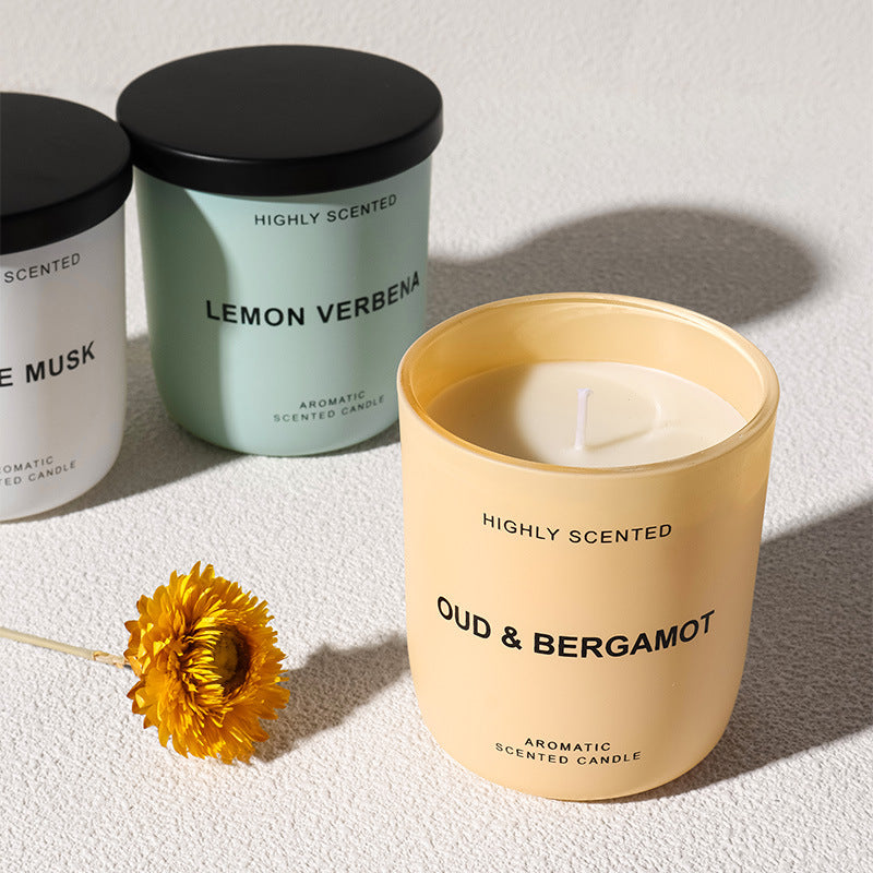 Three scented candles with black lids on a light surface, one of which is 'Oud & Bergamot'.