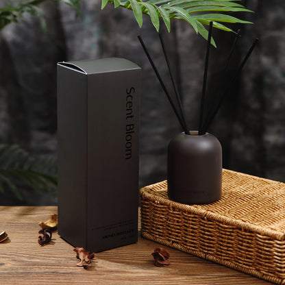 Scent Bloom diffuser with packaging on a wooden surface with a blurred green plant background