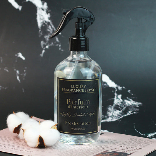 Clear spray bottle with black label on a dark surface with cotton flowers