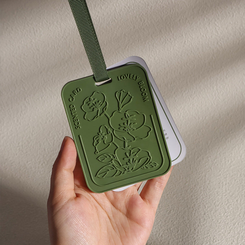 Green scented card with floral designs held by a hand against a beige background