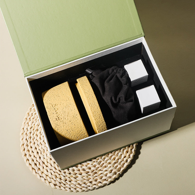 Set of beauty products including sponges and a black cloth in an open box on a woven mat.