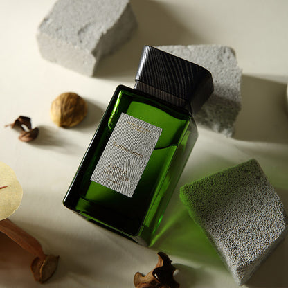 Green bottle with a label on a textured surface with rocks and nuts.