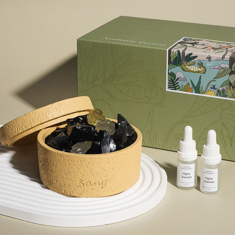 Round beige container with black stones, two white bottles labeled 'Highly Scented', and a green decorative box on a beige surface.