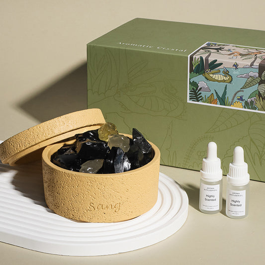 Round beige container with black stones, two white bottles labeled 'Highly Scented', and a green decorative box on a beige surface.